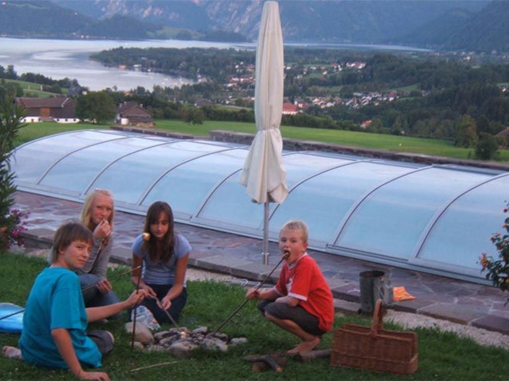Ein Gewächshaus mit Glasdach, einem Picknicktisch und Blick auf einen See und Berge.