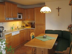 A compact kitchen with wooden cabinets, a microwave, and a dining area with a table and green upholstered chairs.