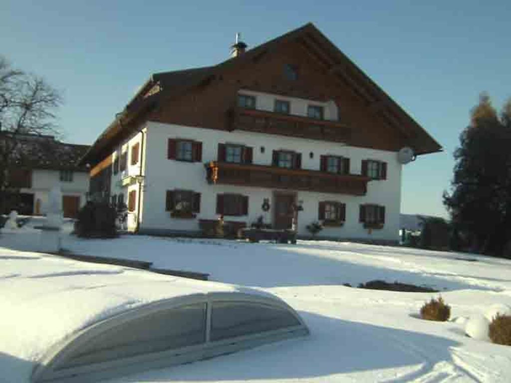 Un edificio de dos pisos con techo inclinado, un balcón en el nivel superior y el suelo cubierto de nieve.