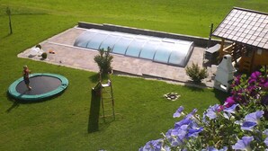 Ein Haus mit einem großen Gewächshaus, einem Trampolin und einem blühenden Garten.