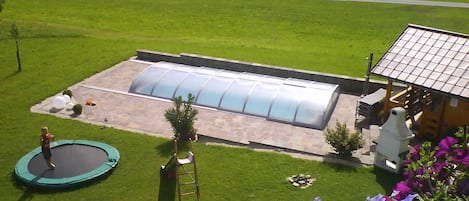 Una casa con un invernadero grande, un trampolín y un jardín lleno de flores.
