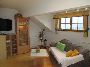 Un salon avec un téléviseur, des meubles en bois, un canapé avec des coussins, une fenêtre avec des rideaux et une plante.