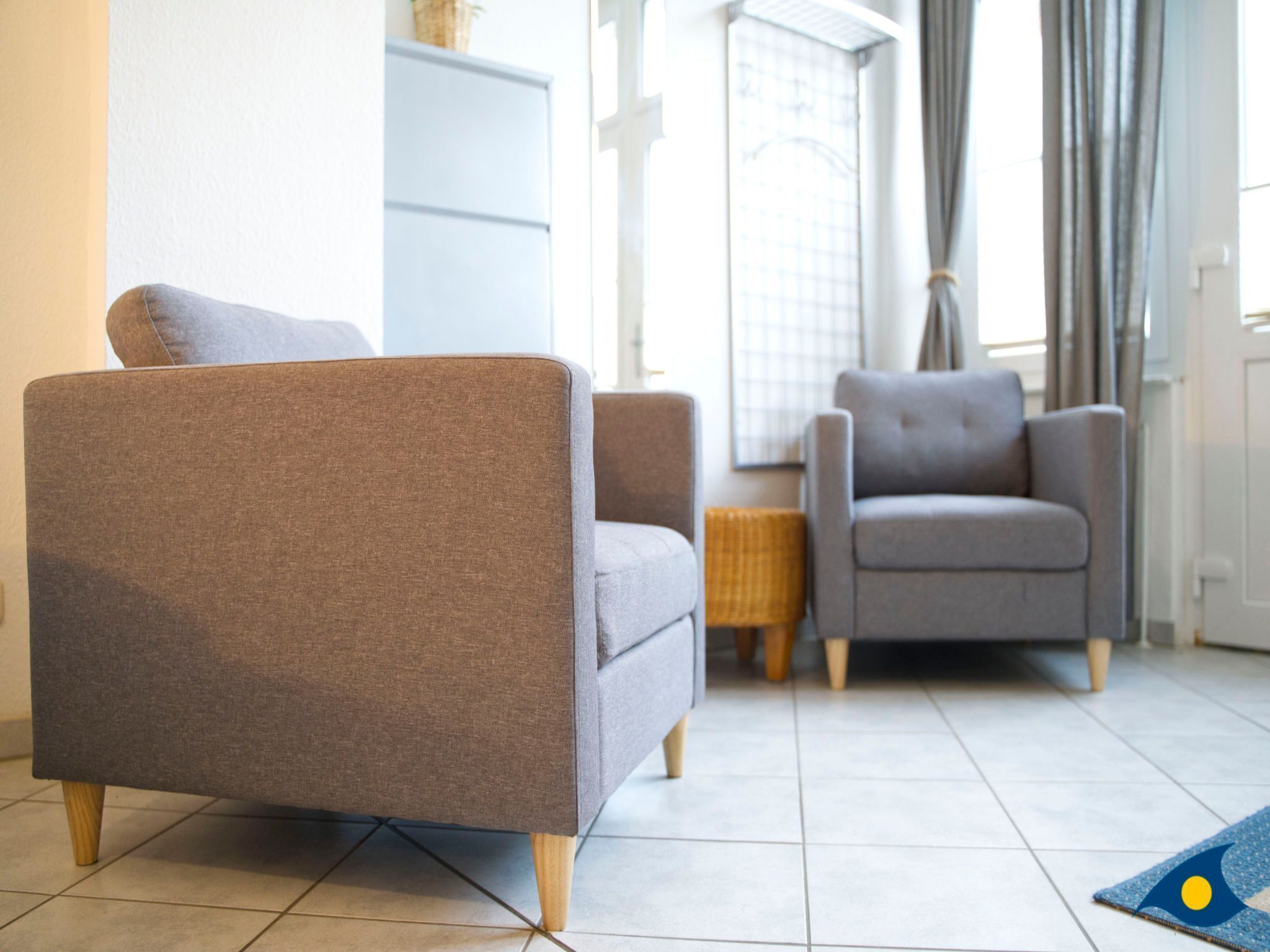 A modern living room with two grey armchairs and a sofa, a small wooden side table, and a blue rug with a yellow design.