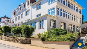 A multi-story building with a white facade, large windows, and a stone wall with greenery in front. - Rolandseck I, Apt. 04 - A Little Oasis Near the Beach - RO I 04 (Heringsdorf)