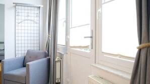 A room with a grey armchair, a radiator, and a window with curtains. - Rolandseck I, Apt. 04 - A Little Oasis Near the Beach - RO I 04 (Heringsdorf)