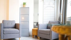 A modern living room with two grey armchairs, a small table, a wicker side table, a tall cabinet, and a window with blinds. - Rolandseck I, Apt. 04 - A Little Oasis Near the Beach - RO I 04 (Heringsdorf)