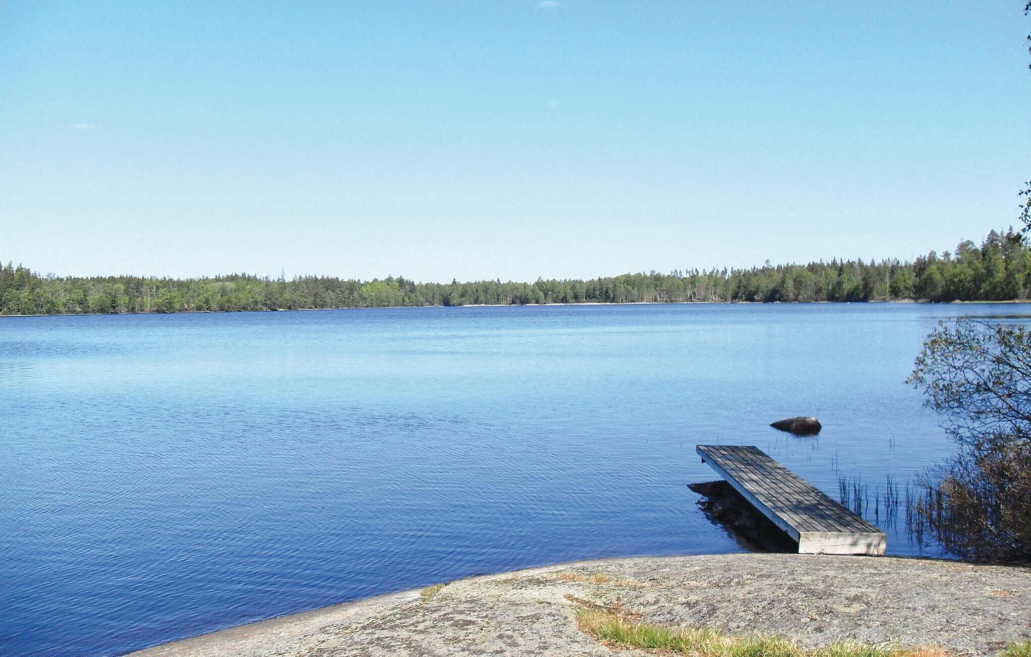 A calm lake with a dock extending into the water, surrounded by a forested shoreline.