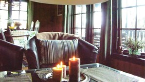 Ein gemütliches Zimmer mit Ledersofa, einem Glastisch mit Kerzen und Blick durch große Fenster.