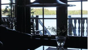 Ein Essbereich mit Tisch für zwei Personen, einer Hängelampe und Blick auf einen See durch große Fenster.