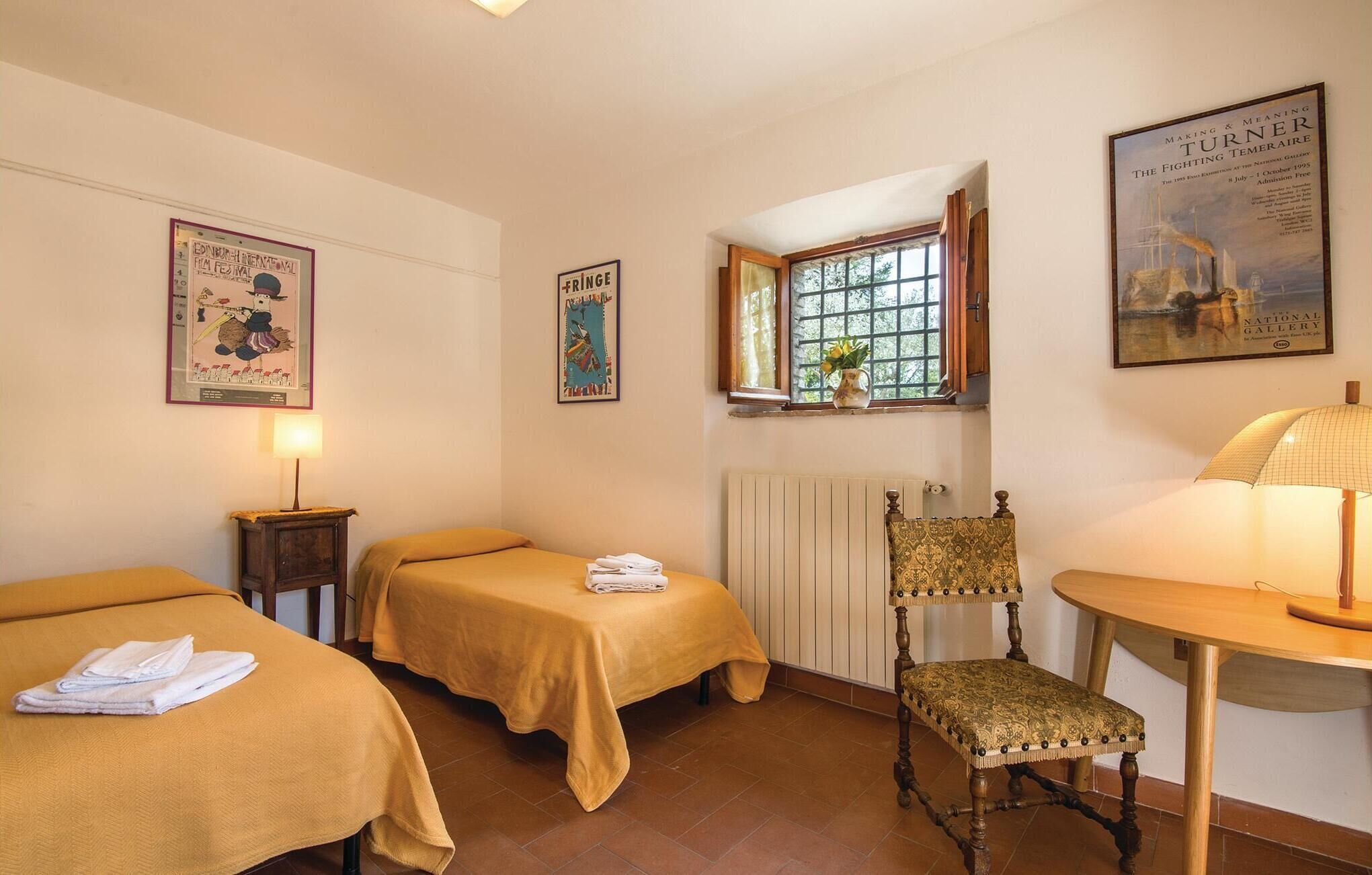 Une pièce avec deux lits, une chaise, une table, une fenêtre et divers tableaux encadrés accrochés aux murs.