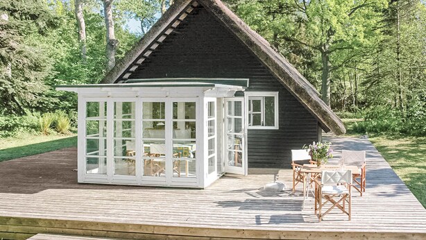 A wooden deck with a glass-enclosed patio area, a small table, and chairs. - 2 bedroom stunning home in Græsted (Græsted)