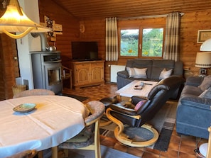 Interior acogedor de una cabaña con sofá, sillas, una mesa, televisor y chimenea.