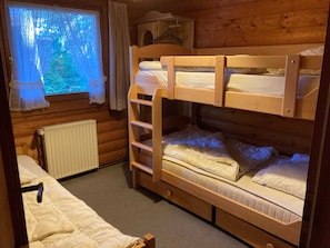 Una habitación de cabaña de madera con literas, una ventana con cortinas y un radiador.