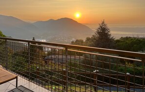 A balcony with a metal railing overlooking a cityscape during sunset.