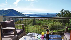 A balcony with wicker furniture, a table, and a bottle of wine, overlooking a scenic view of mountains and a body of water. - Stunning home in Villanuova sul C. BS with outdoor swimming pool (Villanuova sul C. BS)