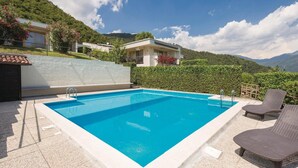 A rectangular swimming pool with a clear blue water, surrounded by a stone deck. There are two wicker lounge chairs and a small table on the right side. - Stunning home in Villanuova sul C. BS with outdoor swimming pool (Villanuova sul C. BS)
