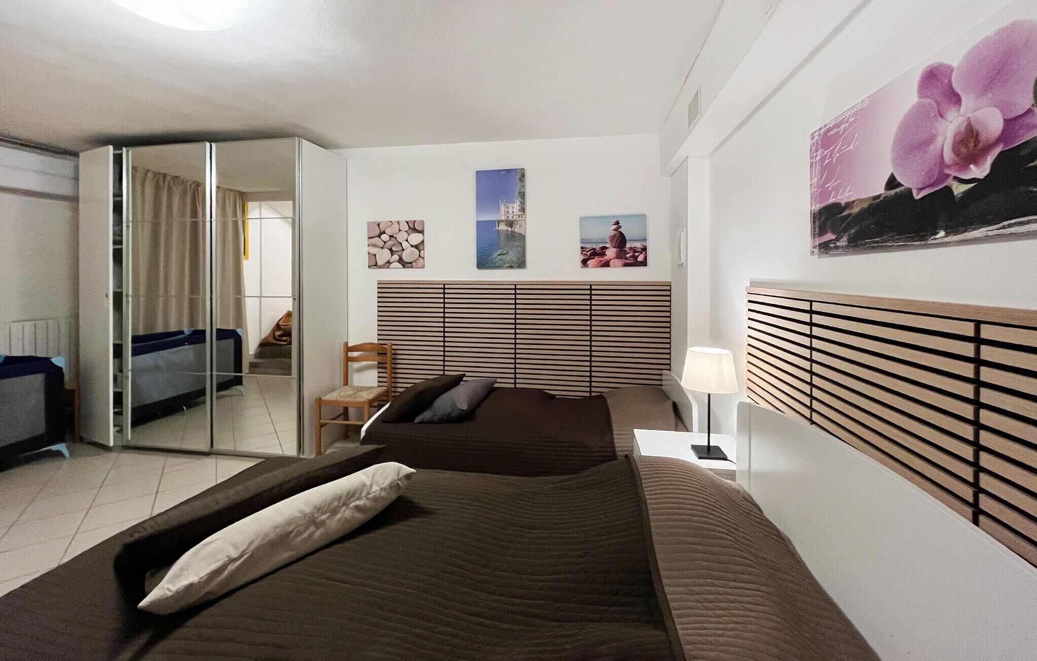 A hotel room with a bed, a chair, a desk with a lamp, and artwork on the walls.