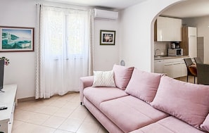 Un salon avec un canapé, un coin repas avec des chaises, une cuisine avec des placards et des appareils électroménagers, et une fenêtre avec des rideaux.