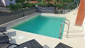 Una piscina rectangular con agua cristalina, rodeada por una solana con baldosas. Hay dos tumbonas y una escalera metálica que da a la piscina.