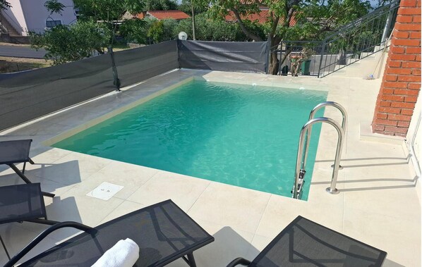 Ein rechteckiger Pool mit klarem Wasser, umgeben von einer gefliesten Liegefläche. Zwei Liegestühle und eine Metallleiter führen in den Pool.