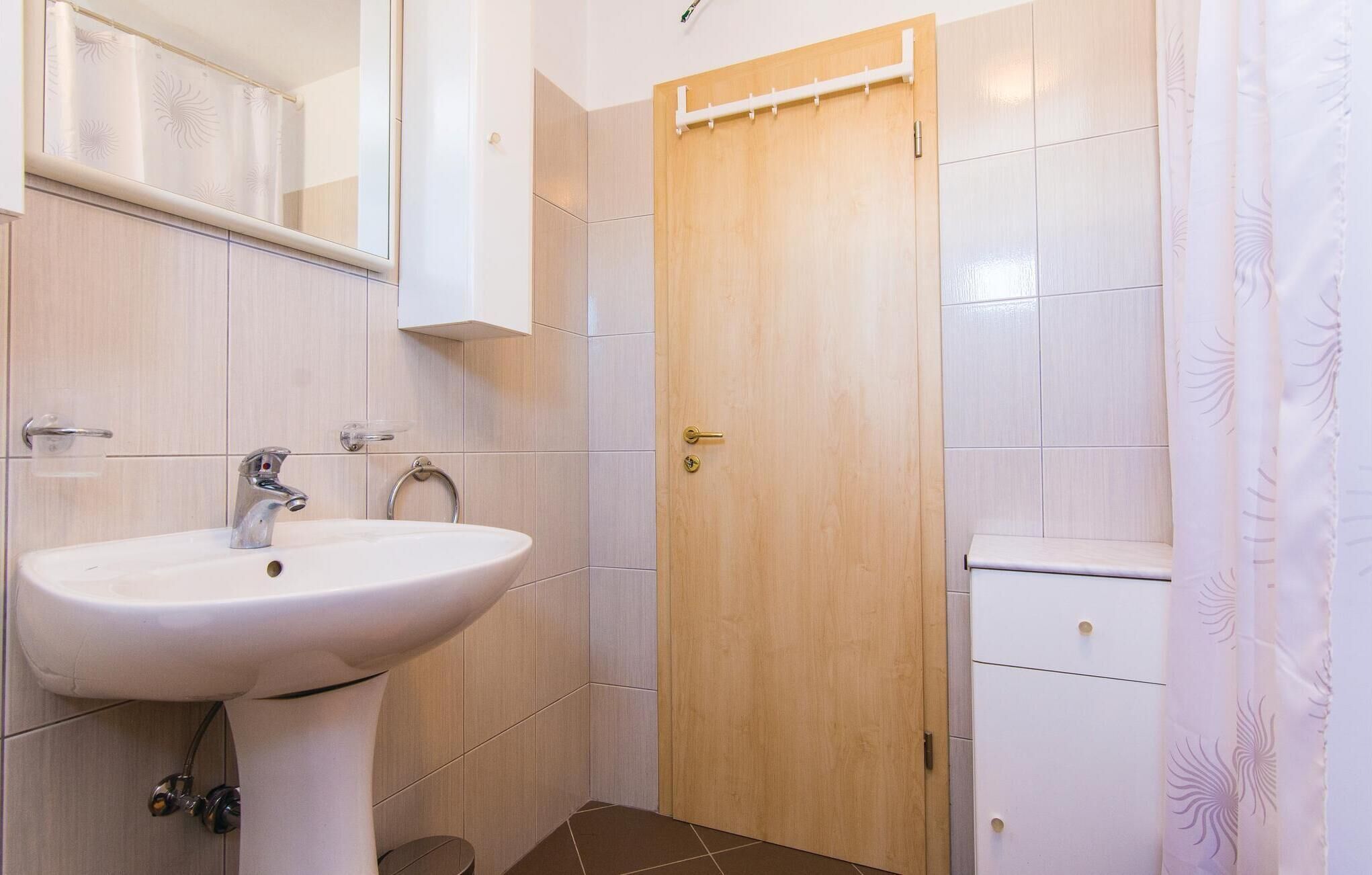 Ein Badezimmer mit weißem Waschbecken, einem Spiegel, einer Holztür und einer Duschvorhang.
