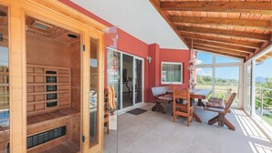 A wooden sauna with sliding glass doors, a wooden table with chairs, and a view of the countryside.