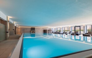An indoor swimming pool with a glass barrier, lounge chairs, and a fireplace. - Stunning apartment in Binz with indoor swimming pool (Prora/Rügen)