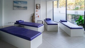 Ein moderner Spa-Raum mit drei Massageliegen, einer Statue und einem Gemälde an der Wand.