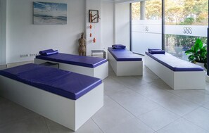 Een moderne spa-ruimte met drie massagetafels, een beeld en een schilderij aan de muur.