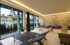 Un espacio interior moderno con ventanas amplias, sillones negros y cojines morados.