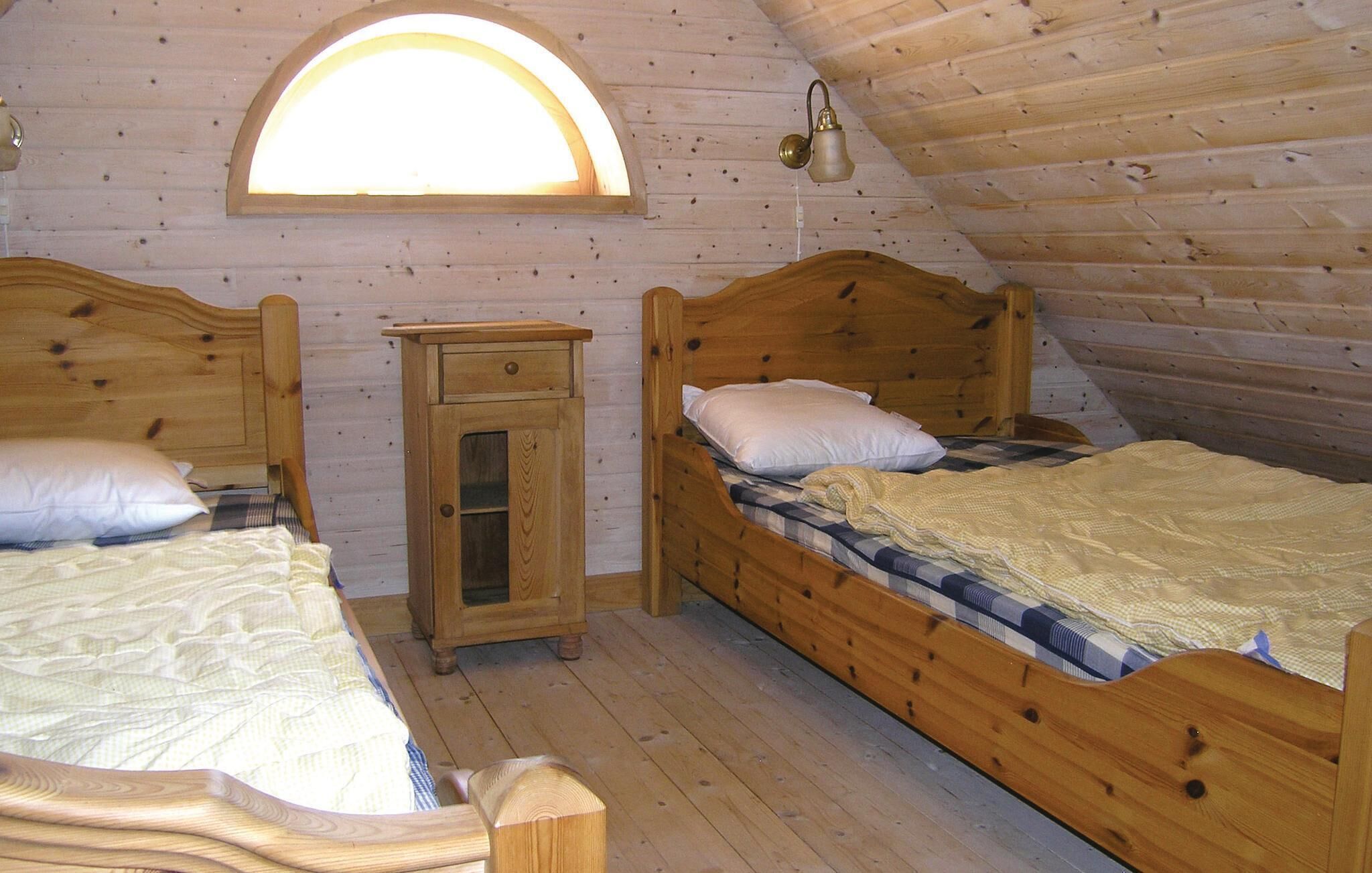 A cozy attic bedroom with two wooden beds, a small wooden cabinet, and a skylight.