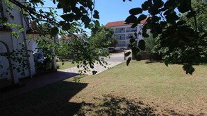 En gårdsplads med en belagt sti, en bygning med rødt tegltag og grøn beplantning omkring.