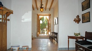 A hallway with a wooden door, a dining area with chairs and a table, and a bed with a headboard.