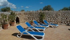 A sunbathing area with lounge chairs and potted plants, set against a stone wall and clear sky.