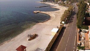 Une route côtière bordée d’une plage en arc de cercle, d’une structure en bois et offrant une vue dégagée sur la mer.