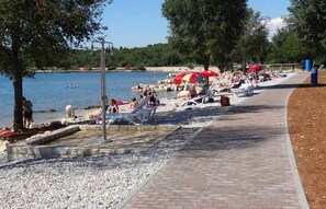Una spiaggia con persone che si rilassano, un vialetto e una distesa d'acqua.