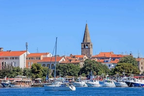 Un port avec des bateaux, un clocher dâĂ©glise et des bĂątiments aux toits recouverts de tuiles rouges.