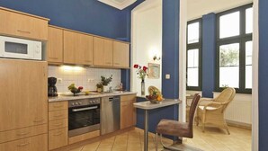 A modern kitchen with wooden cabinets, stainless steel appliances, and a dining area with a wicker chair and a table. - Apartment Stephanie - House Prussia (Heringsdorf)