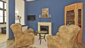 A living room with blue walls, a fireplace, two armchairs, a glass table, and a wooden cabinet. - Apartment Stephanie - House Prussia (Heringsdorf)