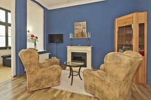 Un salon aux murs bleus, avec une cheminée, deux fauteuils, une table en verre et un meuble en bois.