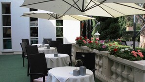 An outdoor patio with tables and chairs, covered by large umbrellas, and a flower bed with various flowers.