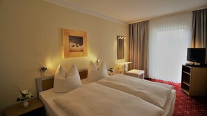 A hotel room with a large bed, a TV, a desk, and a painting on the wall.