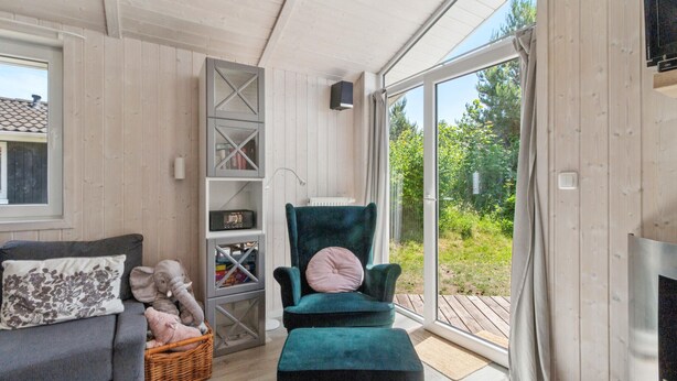 Un salon chaleureux avec un fauteuil vert foncé, un canapé gris et un panier en osier rempli de peluches.