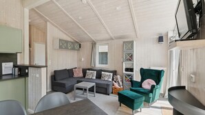 Un salon chaleureux avec un canapé gris, un fauteuil vert et une petite table. Il y a également un coin cuisine avec un comptoir et des placards.