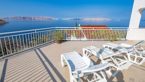 Un balcon avec des chaises blanches et un pot de fleurs, d’où l’on peut admirer une mer calme et des montagnes lointaines.