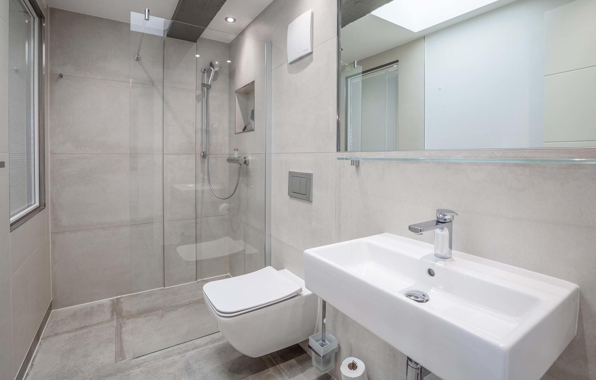 Un baño moderno con cabina de ducha de vidrio, inodoro blanco y un lavamanos grande con un espejo encima.