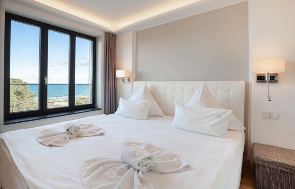A hotel room with a large bed, two bedside lamps, a view of the sea, and a neatly made bed with towels. - Beautiful apartment in Binz with outdoor swimming pool (Prora/Rügen)