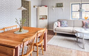 Een eetgedeelte met een houten tafel en stoelen, een bank met kleurrijke kussens en behang met een patroon.