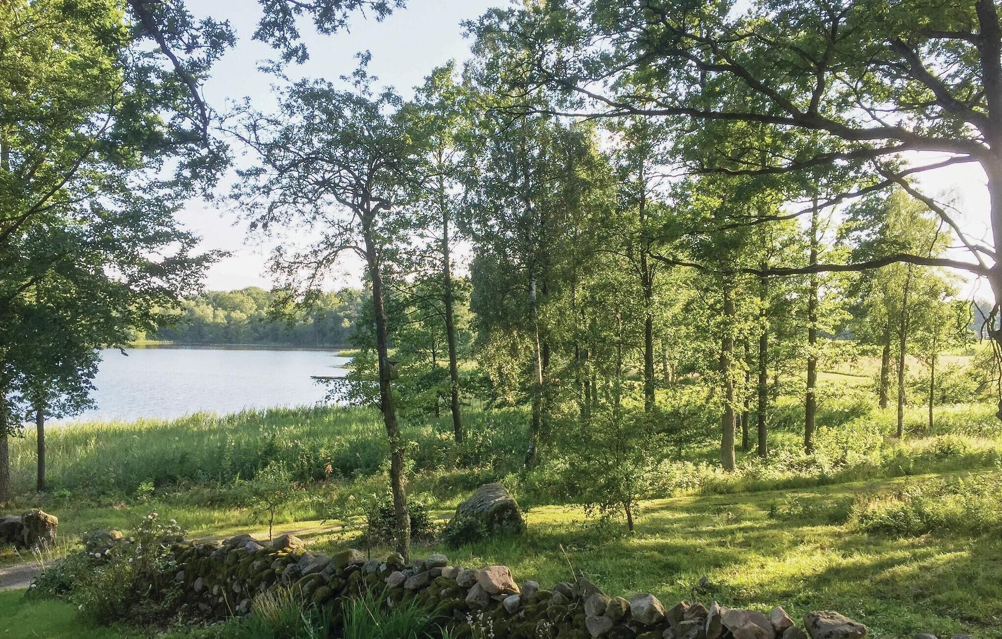Paisagem natural com um lago, árvores e um muro de pedra.