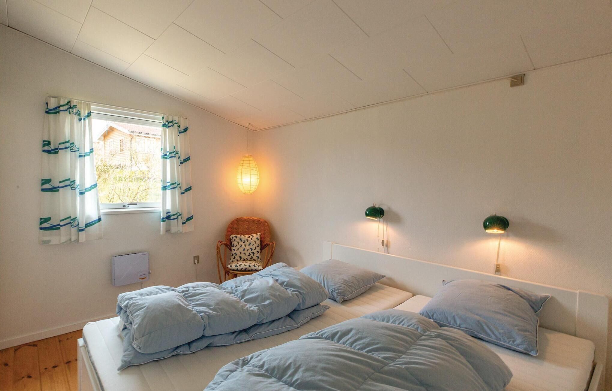 A bedroom with a bed, two bedside lamps, a chair, and a window with curtains.